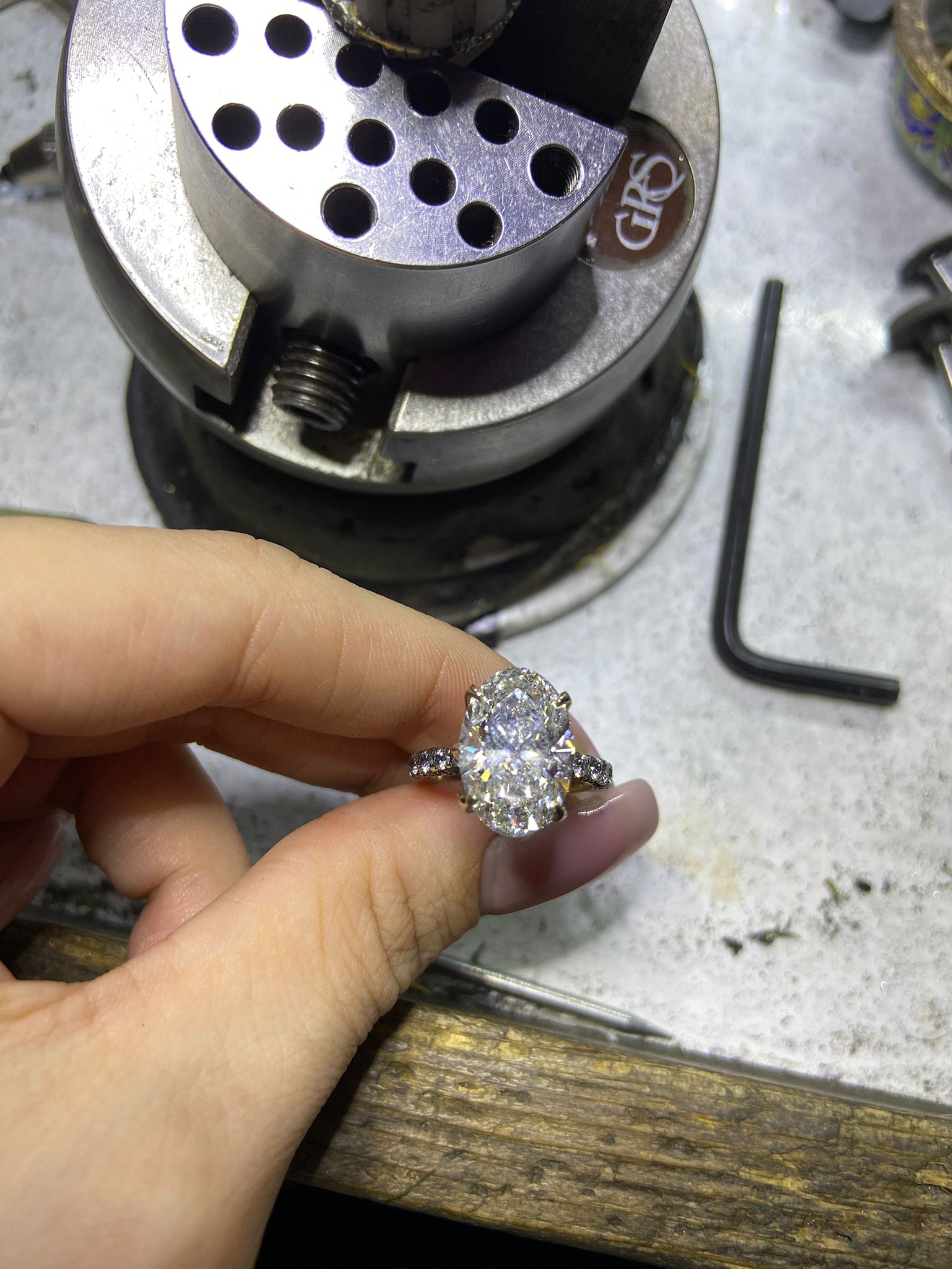 Diamond ring held by a hand with a jewelry-making tool in the background